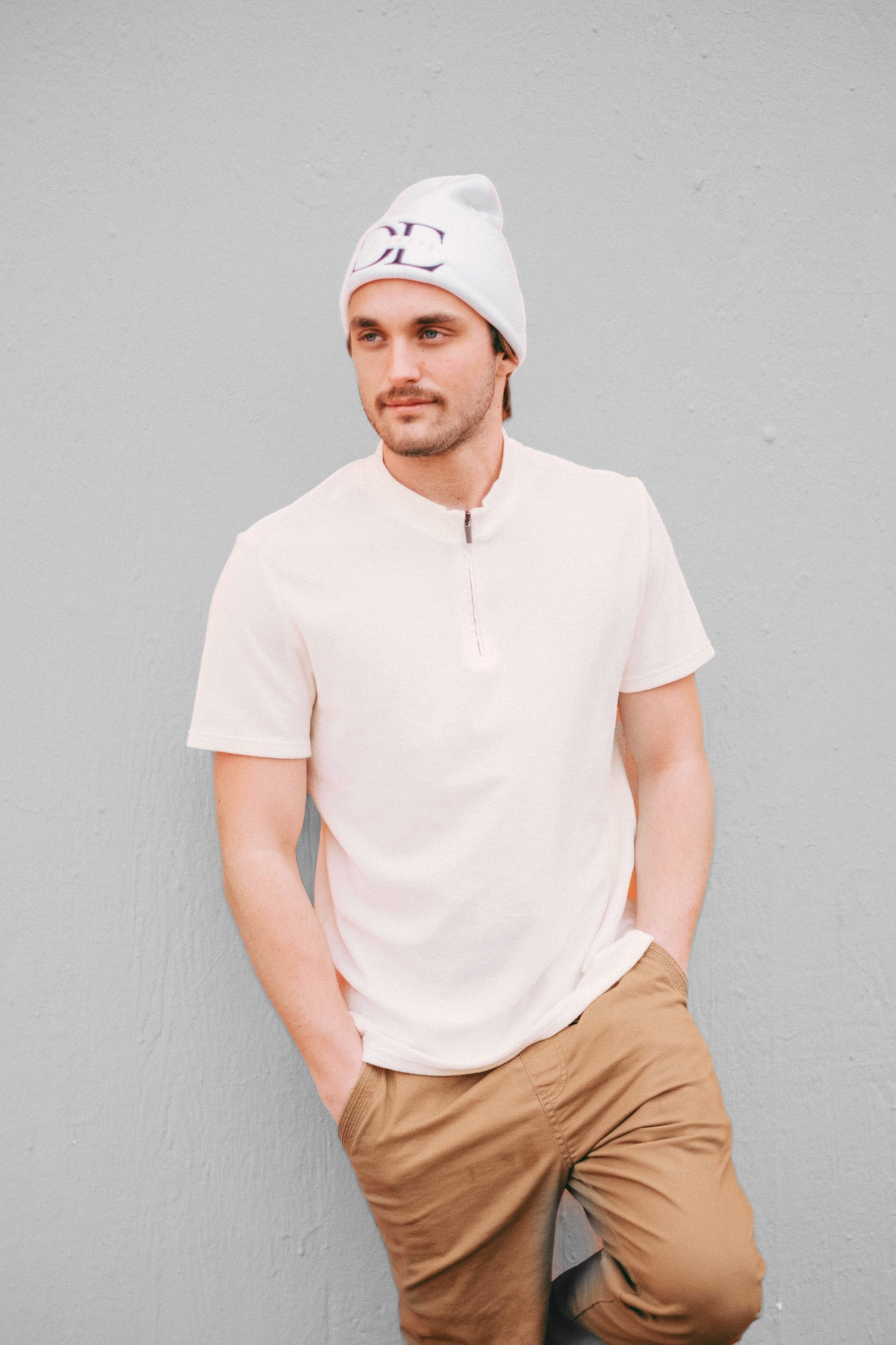 frontal image of White Die Empty Beanie on a caucasian male model taken from a frontal angle with full body showing, model has a white tshirt and khaki pants and has his hands in his pockets